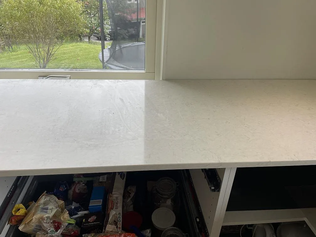 Rak bänkrad i polerad Silestone Snowy Ibiza framför stort köksfönster med trädgårdsutsikt i Olofstorp.