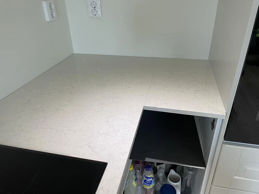 Hörnparti av polerad Silestone Snowy Ibiza vid svart induktionshäll, vita stommar och högskåp i Olofstorp.