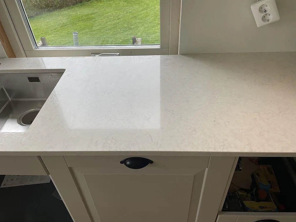 Polerad Silestone Snowy Ibiza bänkskiva vid fönster med synlig ljusgrå ådring och rostfri diskho i Olofstorp.