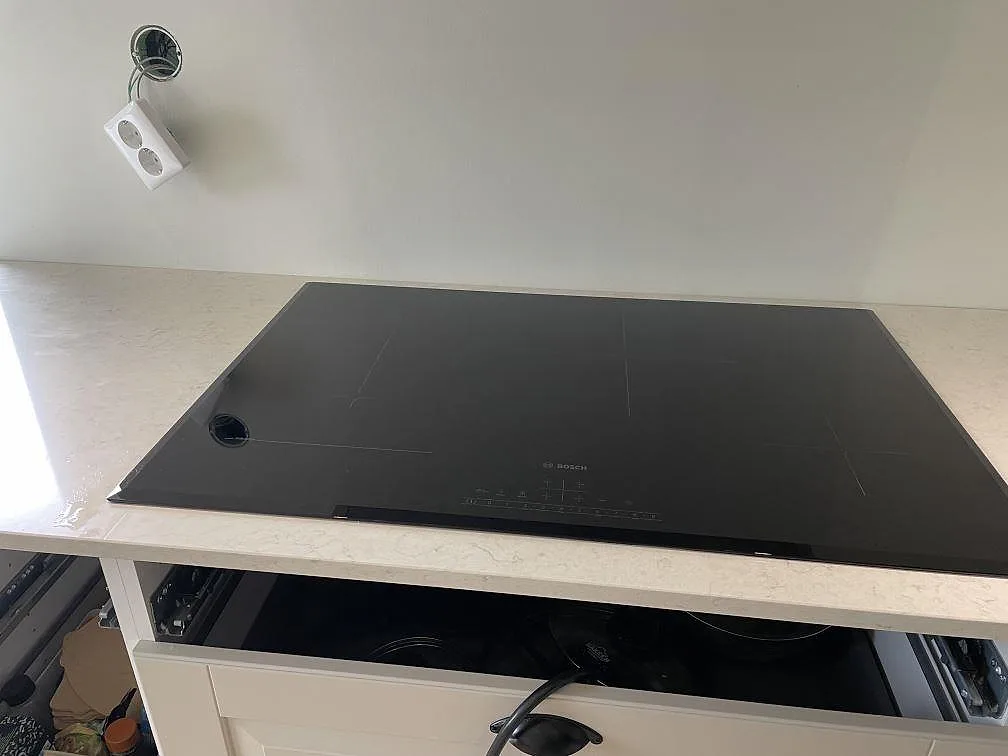 Svart induktionshäll infälld i en polerad Silestone Snowy Ibiza köksbänkskiva under montering i Olofstorp.