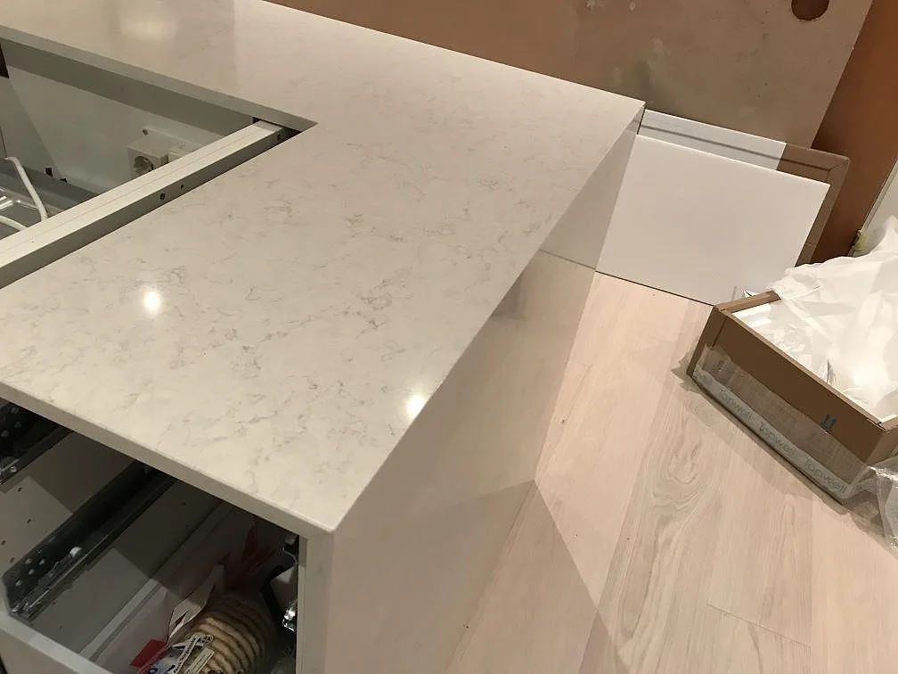 L-formad bänkrad i Silestone Snowy Ibiza med urtag för häll och polerad stenyta i ett kök i Onsala.
