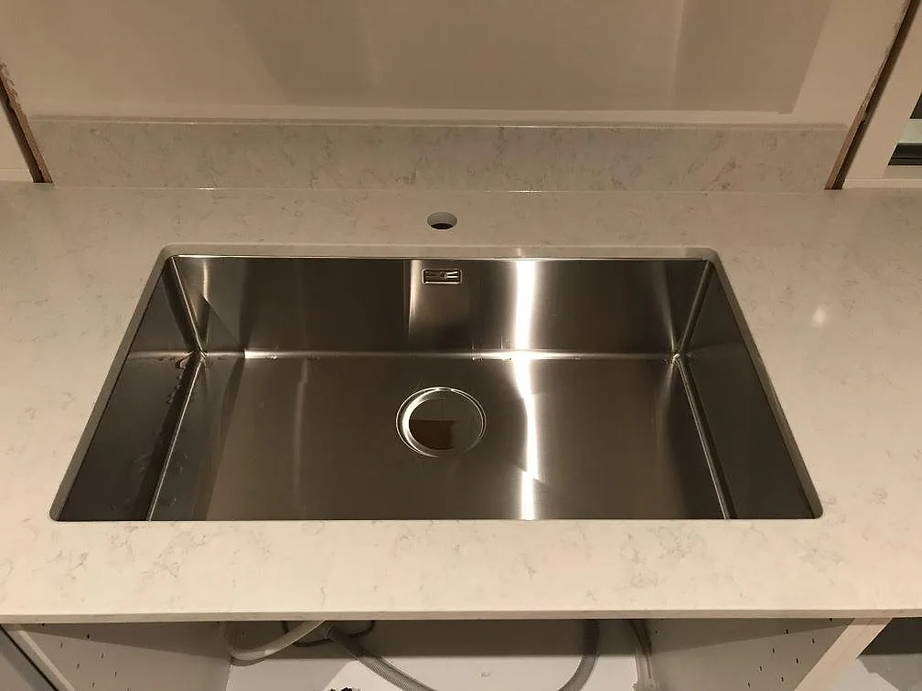 Stor underlimmad rostfri diskho i polerad Silestone Snowy Ibiza med stänkskydd bakom i ett kök i Onsala.