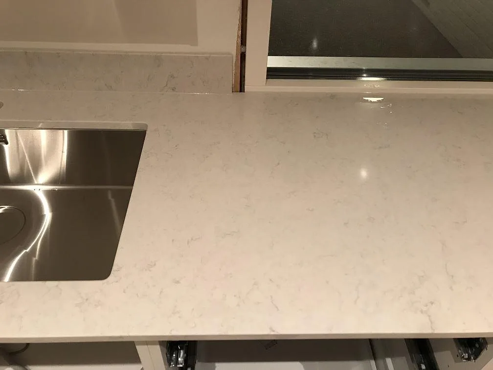 Polerad bänkskiva i Silestone Snowy Ibiza med underlimmad rostfri diskho längs fönsterväggen i ett kök i Onsala.
