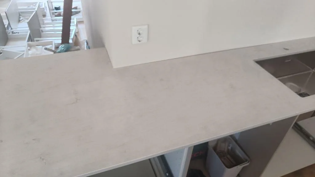 Lång bänkyta i polerad Silestone Snowy Ibiza, ljus kvartskomposit, med diskho vid kanten på öppna köksstommar i Osby.