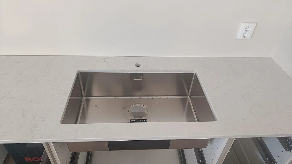 Köksbänkskiva i polerad Silestone Snowy Ibiza, ljus kvartskomposit, med rostfri diskho och separat blandarhål vid väggen i Osby.
