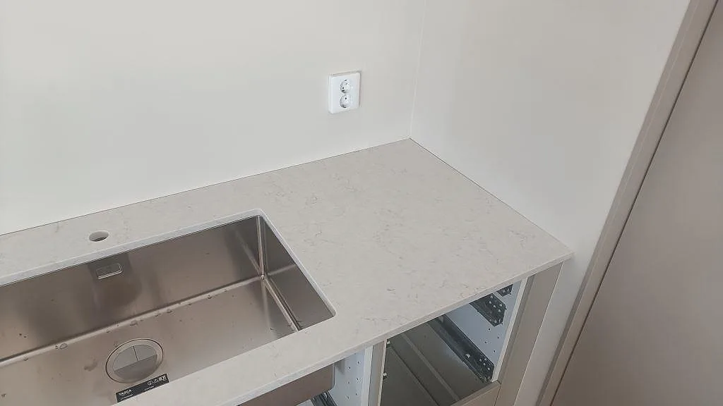 Hörnvy av polerad Silestone Snowy Ibiza, ljus kvartskomposit, med rostfri diskho i ett kök i Osby.