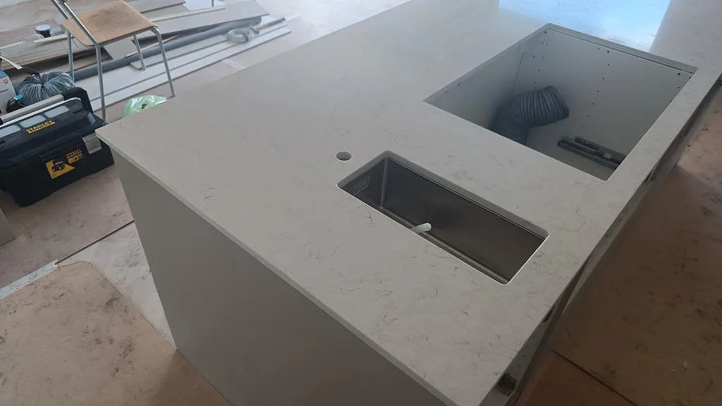 Polerad Silestone Snowy Ibiza som köksbänkskiva i ljus kvartskomposit med rostfri diskho och stort rektangulärt urtag i Osby.