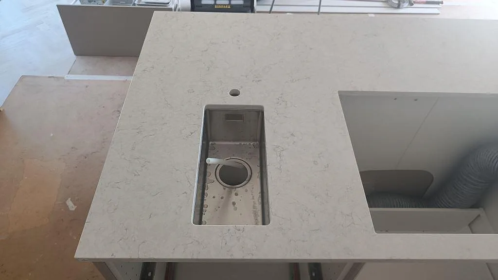Närbild av polerad Silestone Snowy Ibiza i ljus kvartskomposit med liten rostfri diskho och större urtag på köksbänken i Osby.