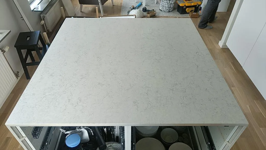 Stort köksö i polerad Silestone Snowy Ibiza ovanifrån, kvartskomposit i ett kök under montering i Oxie.