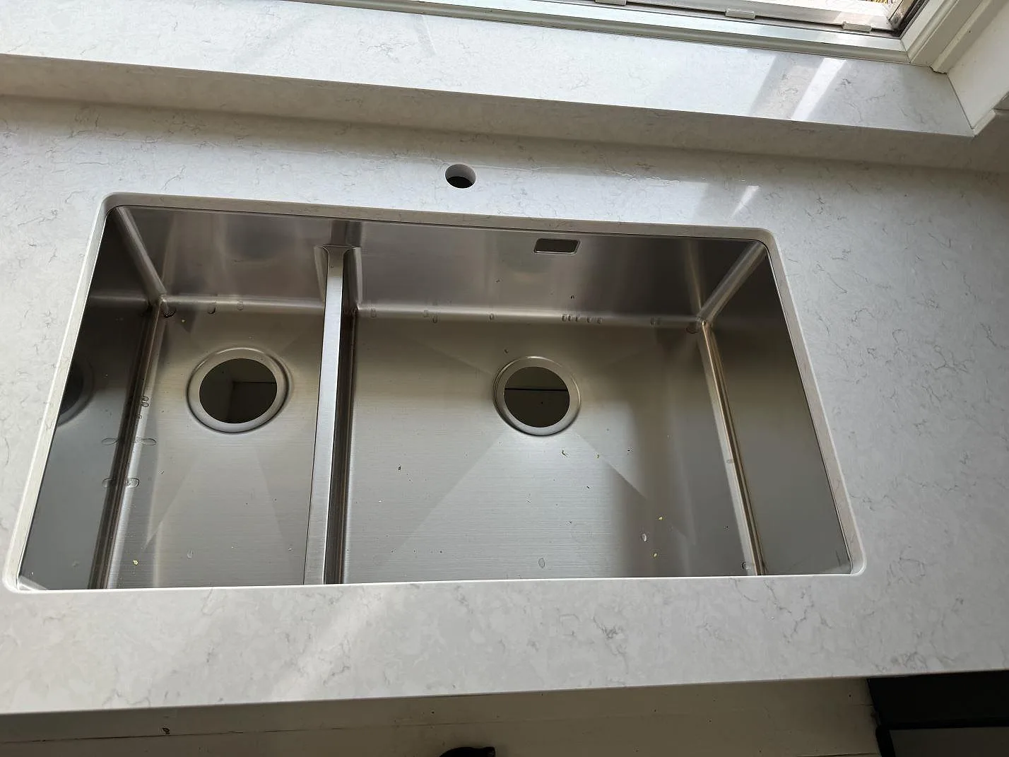 Detalj av rostfri dubbelho i en polerad Silestone Snowy Ibiza köksbänkskiva med fönsterbänk i samma sten i Partille.