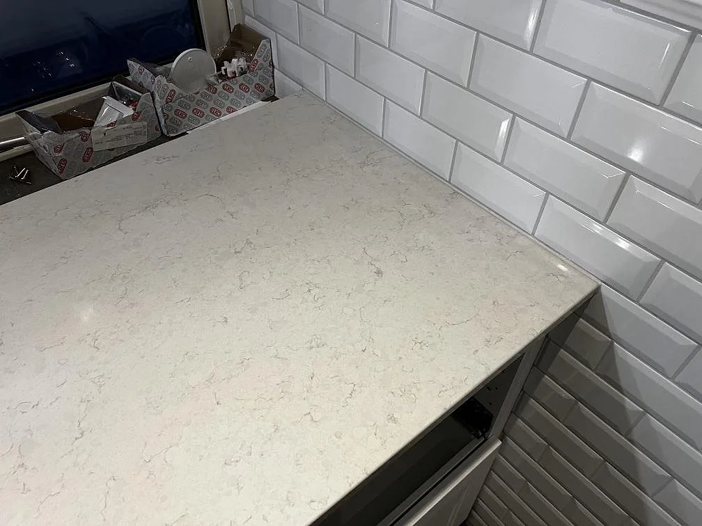 Hörnvy av polerad Silestone Snowy Ibiza som badrumsbänkskiva mot vitt fasat kakel i Röke.