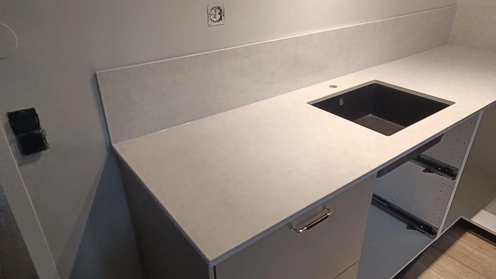 Närbild på polerad Silestone Snowy Ibiza som köksbänkskiva med låg stänkkant och mörk diskho i Rydebäck.