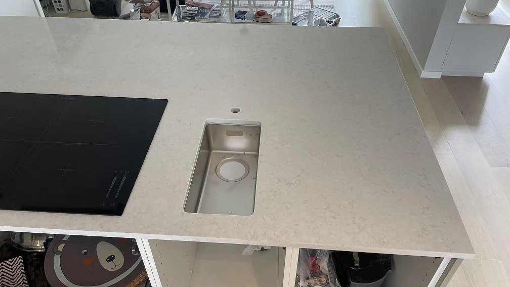 Topvy av köksö i polerad Silestone Snowy Ibiza med svart induktionshäll och underlimmad rostfri diskho i ett kök i Rydebäck.