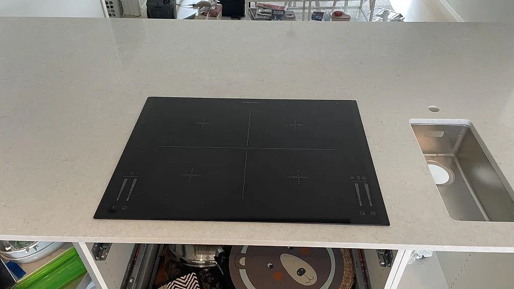 Närbild på svart induktionshäll och rostfri diskho i ljus Silestone Snowy Ibiza, polerad kvartskomposit, i Rydebäck.