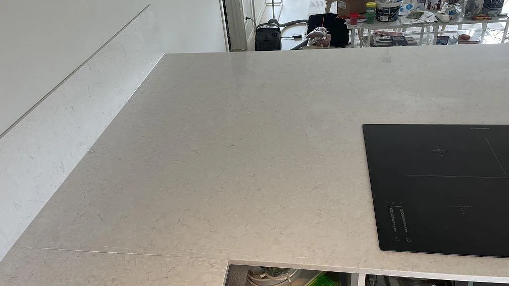 Polerad Silestone Snowy Ibiza på köksö med diskret gråbeige ådring, svart häll och matchande låg stänkkant i Rydebäck.