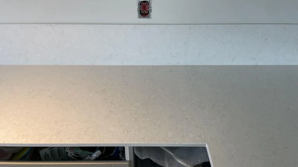 Detalj av polerad Silestone Snowy Ibiza bänkskiva med matchande låg stänkkant och öppna köksstommar under montering i Rydebäck.