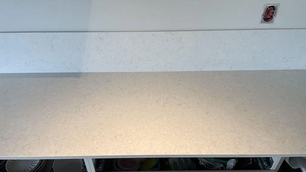 Ljus köksbänkskiva i polerad Silestone Snowy Ibiza med fin gråbeige ådring och låg stänkkant längs väggen i Rydebäck.
