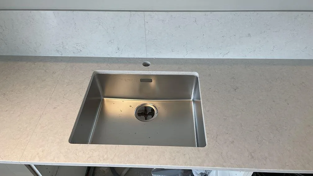Underlimmad rostfri diskho monterad i polerad Silestone Snowy Ibiza med matchande stänkkant bakom bänken i Rydebäck.