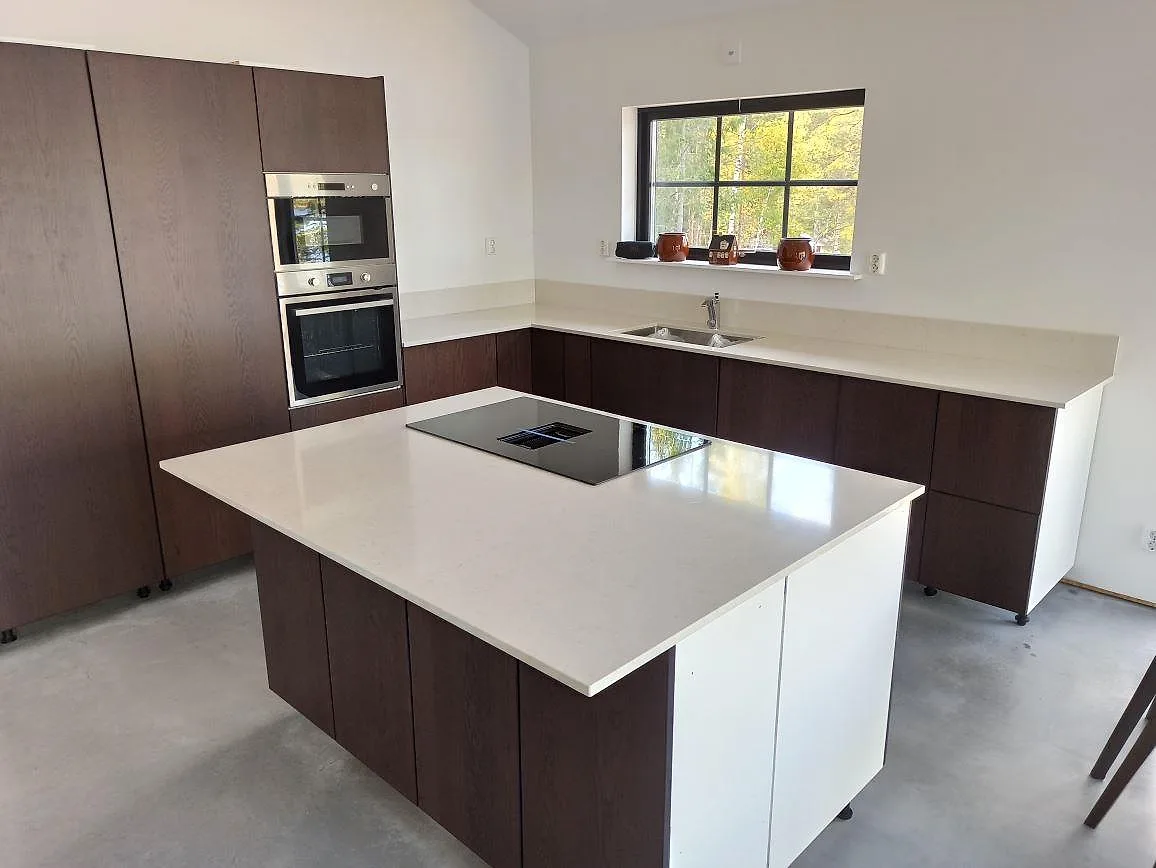 Köksbänkskiva och köksö i vit Silestone Snowy Ibiza, polerad komposit, med induktionshäll i ett kök i Säter.