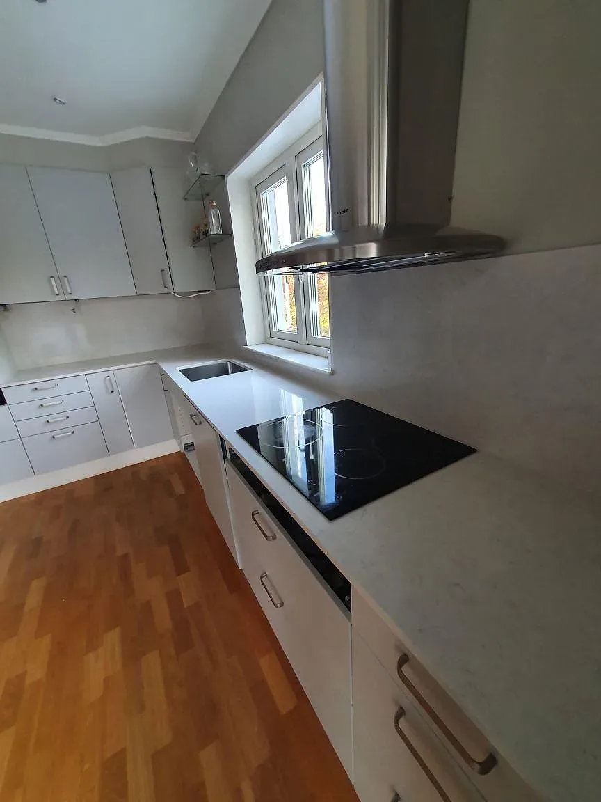 Köksbänkskiva i Silestone Snowy Ibiza, polerad, vid köksfönstret med induktionshäll i ett kök i Saltsjö-Boo.