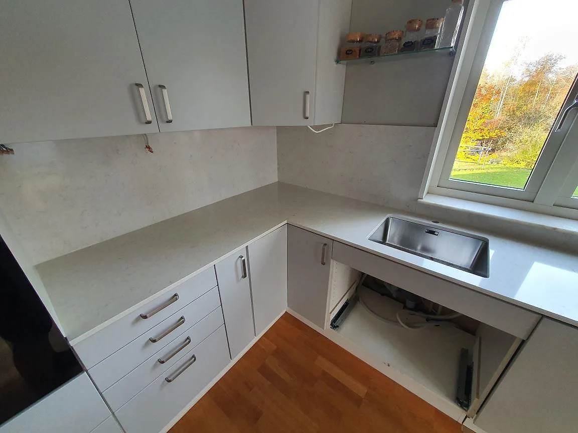 Hörnbänk i vit Silestone Snowy Ibiza, polerad, med underlimmad rostfri diskho och uppvikt stänkkant i ett kök i Saltsjö-Boo.