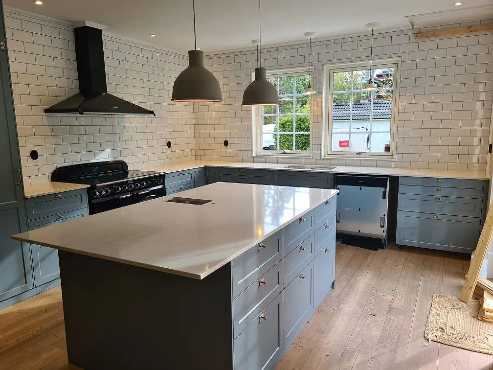 Köksbänkskiva och köksö i polerad Silestone Snowy Ibiza komposit i ett grått kök i Saltsjö Boo.