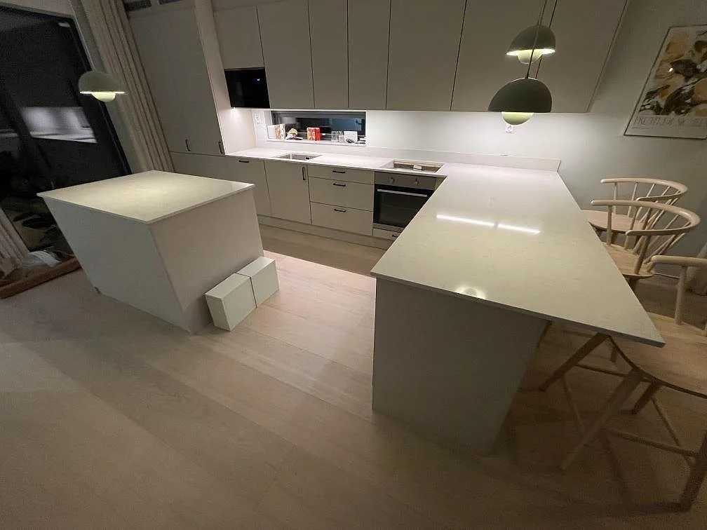 Översikt över kök med polerad Silestone Snowy Ibiza på väggbänk, köksö och stor arbetsyta med stolar i Saltsjö Boo.