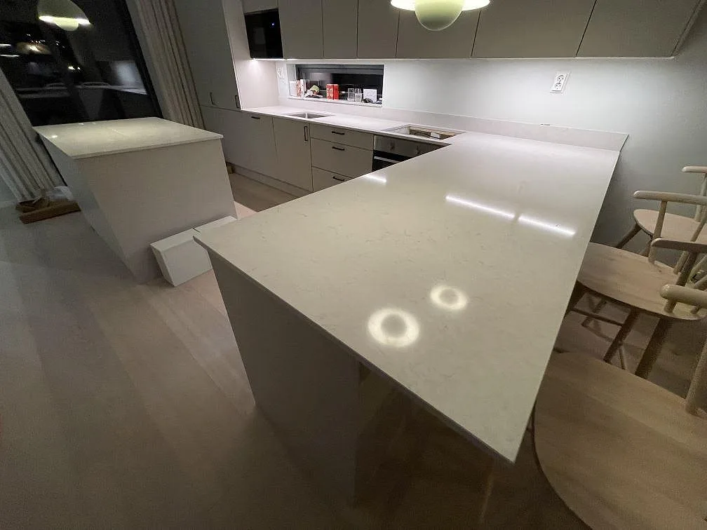 Stor polerad köksskiva i Silestone Snowy Ibiza komposit med ljus ådring, köksö och stänkskydd i Saltsjö Boo.
