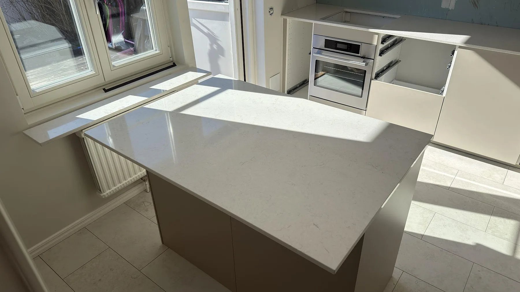 Polerad köksö i Silestone Snowy Ibiza som fångar dagsljuset, med smal fönsterbänk i samma sten, i ett kök i Segeltorp.