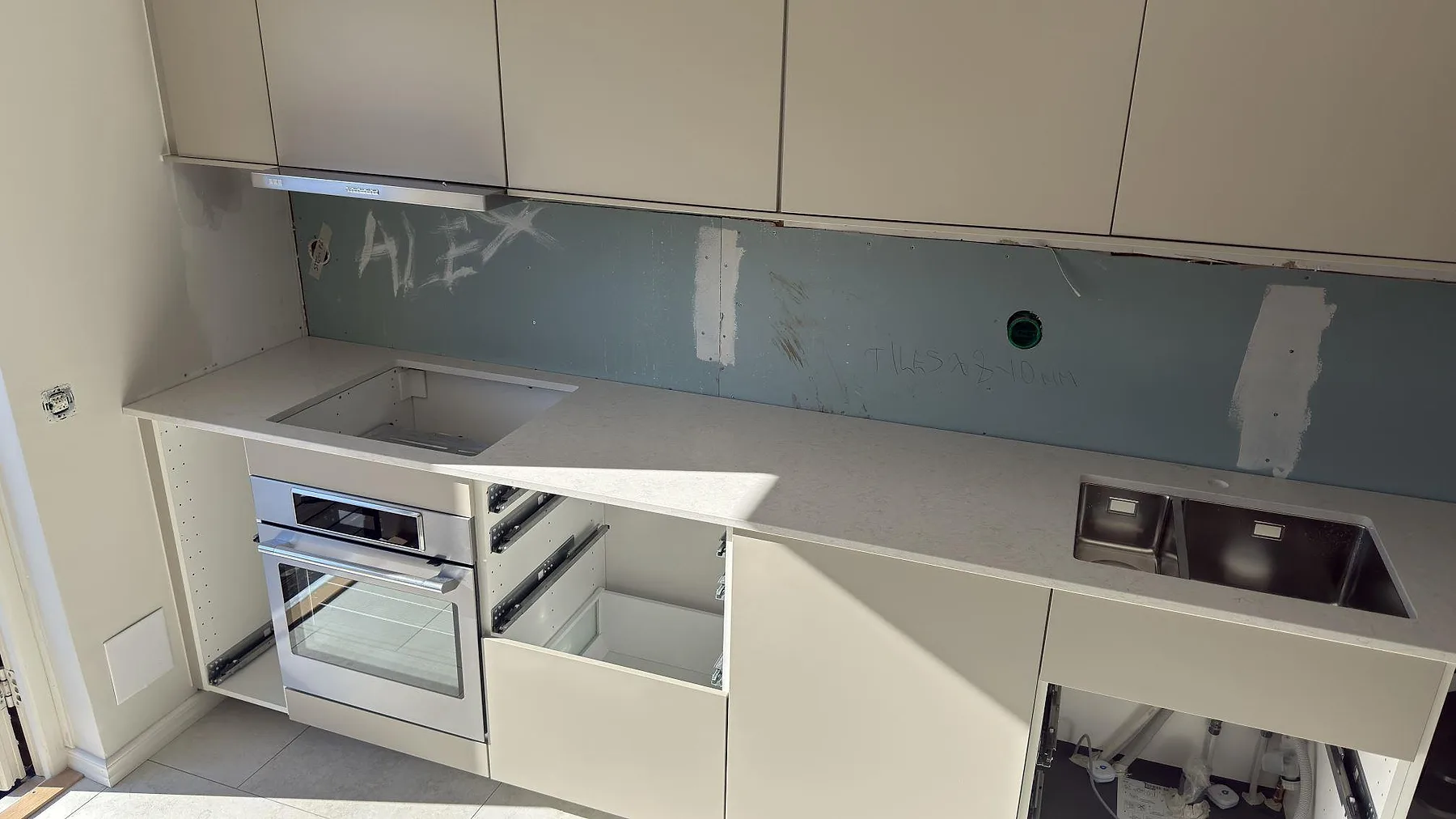 Vinklad köksbänk i Silestone Snowy Ibiza med underlimmad rostfri diskho och ett urtag förberett för häll, intill inbyggd ugn, i ett kök i Segeltorp.