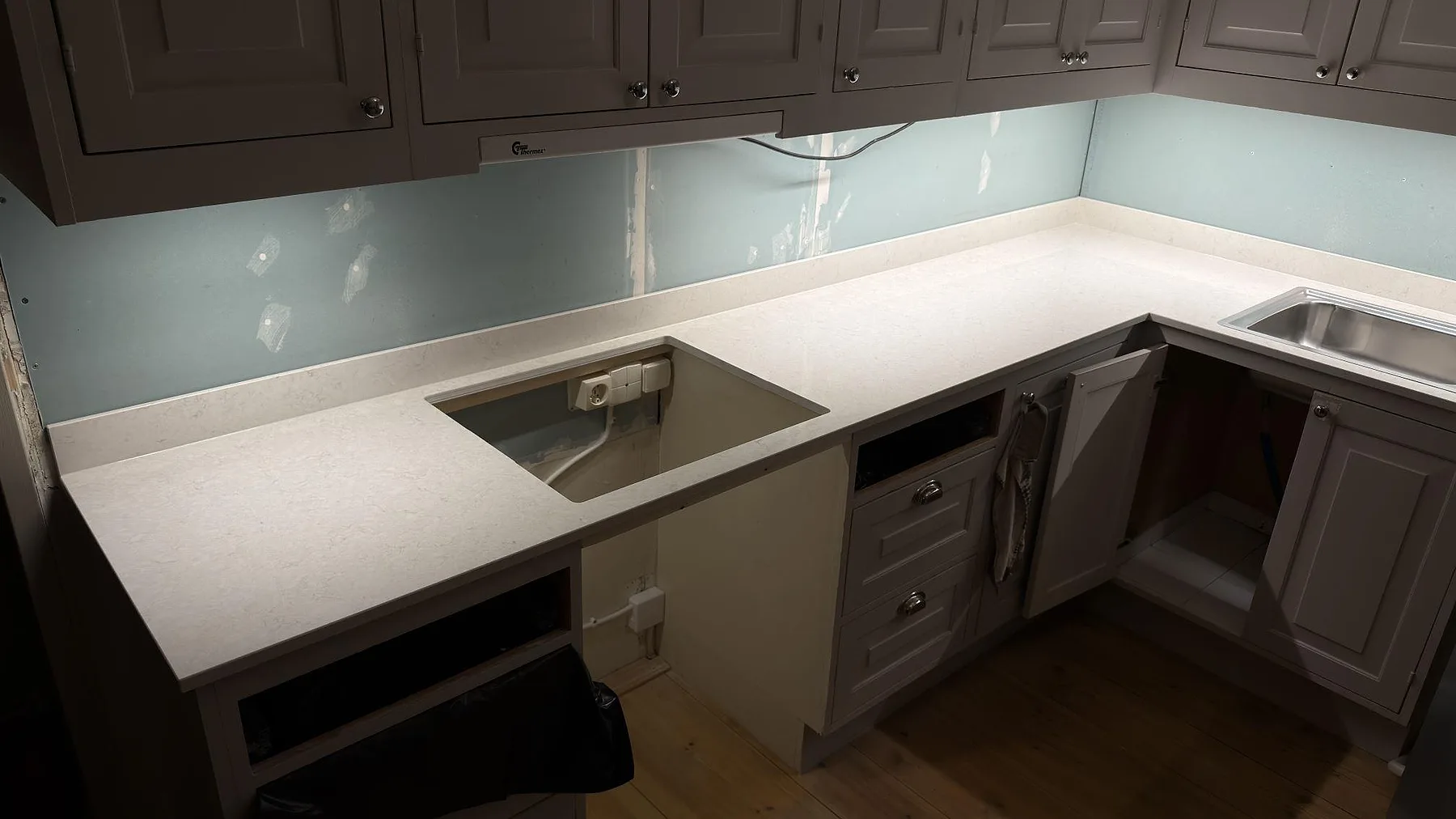 Vit Silestone Snowy Ibiza köksbänkskiva med urtagning för häll och ljusblått glasstänkskydd i ett kök under montering i Sigtuna.