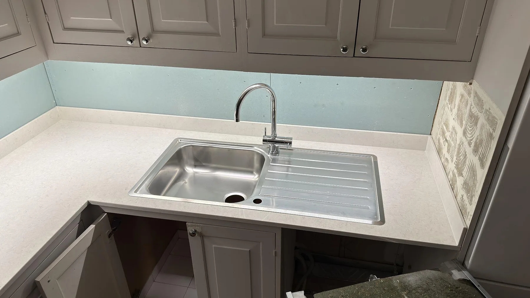 Rostfri nedfälld diskho med rännbräda och krommad blandare ovanpå polerad Silestone Snowy Ibiza i ett kök i Sigtuna.