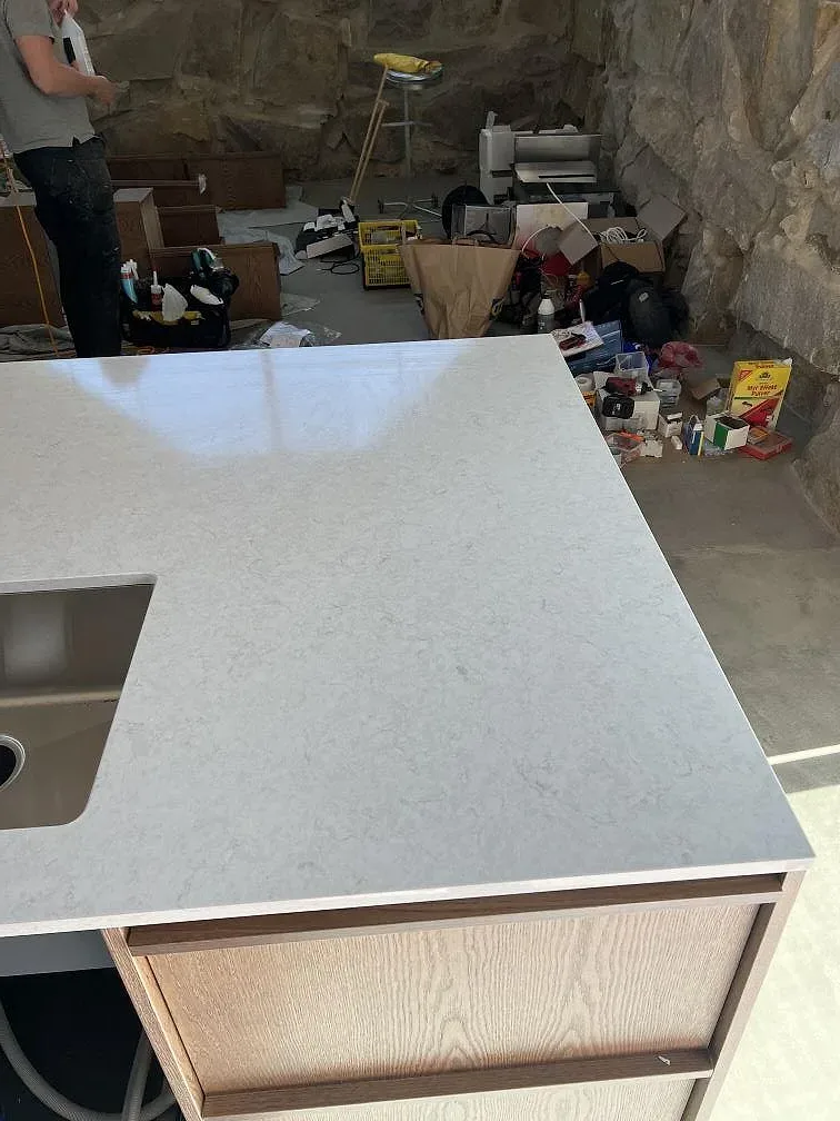 Polerad köksbänkskiva i Silestone Snowy Ibiza på trästommar, fotograferad under montering mot naturstensvägg i Simrishamn.