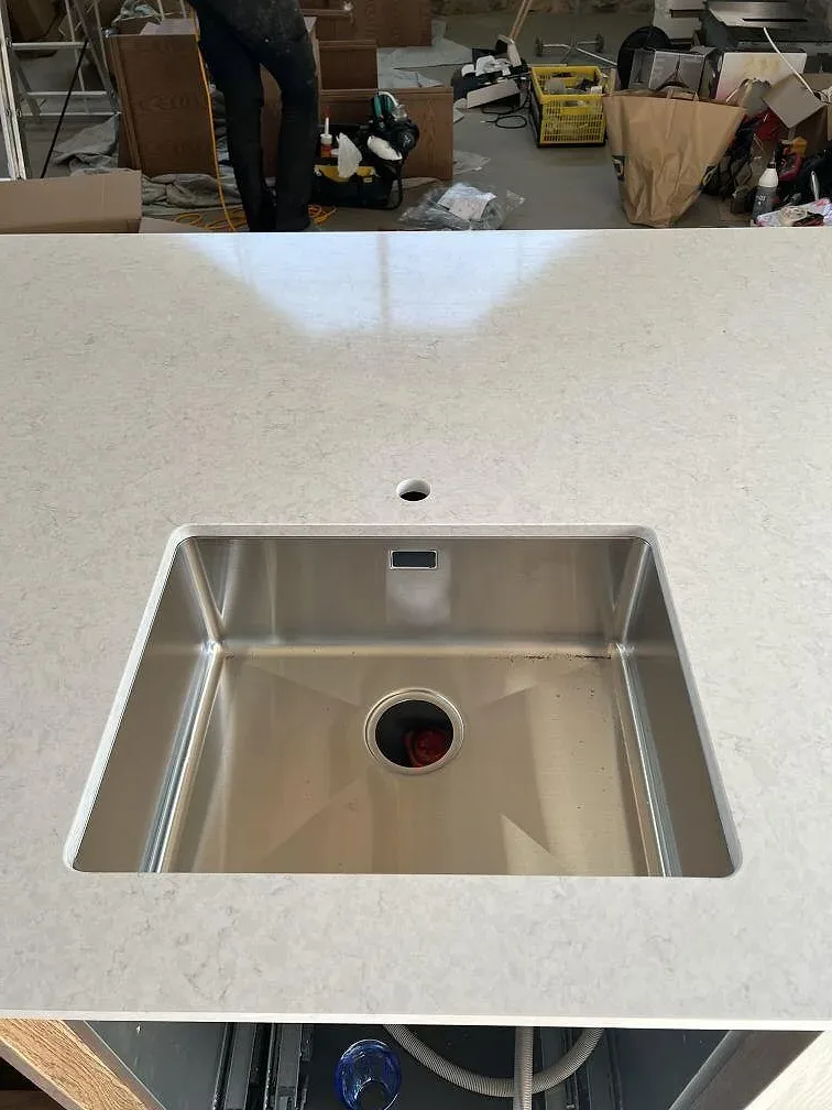 Närbild på polerad Silestone Snowy Ibiza med underlimmad rostfri diskho och blandarhål i köket i Simrishamn.