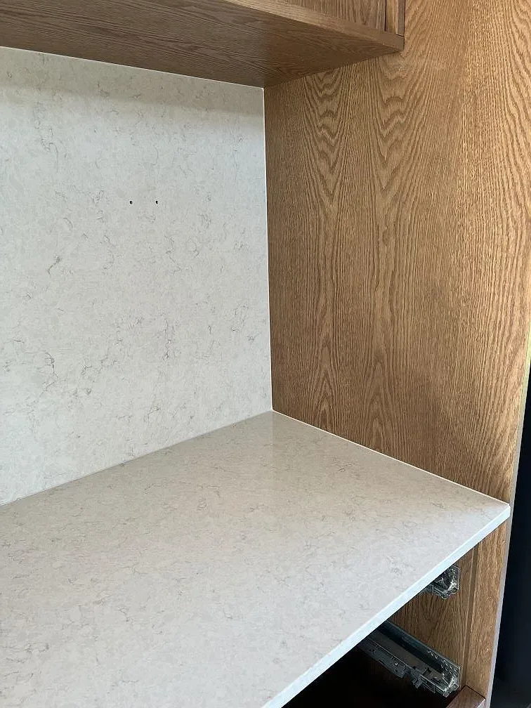 Detalj av Silestone Snowy Ibiza som bänkyta och vertikal stenpanel vid träinredning i köket i Simrishamn.