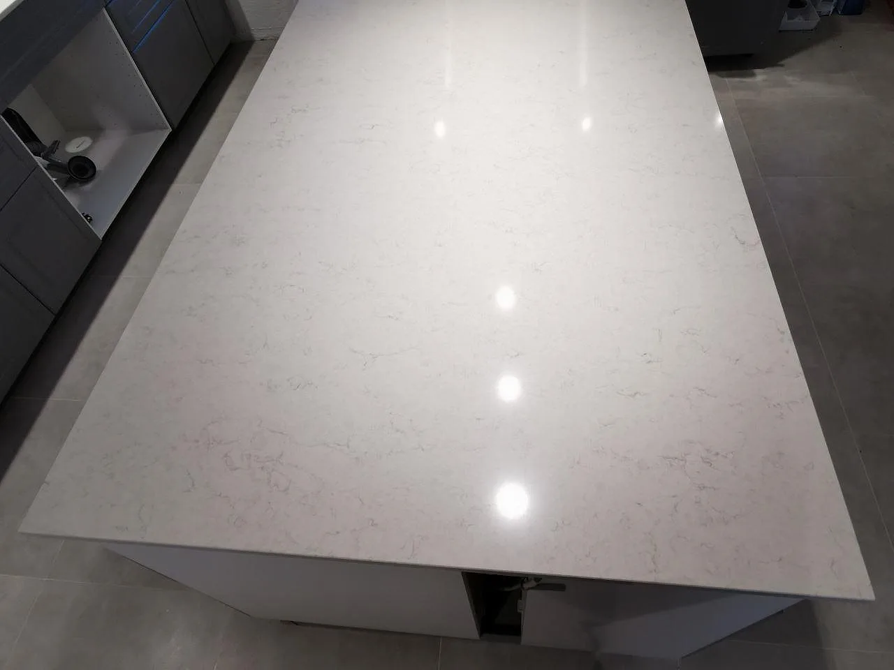Polerad köksö i vit Silestone Snowy Ibiza med diskret grå ådring och spegelblanka takspotlight-reflektioner i ett kök i Sjöbo.