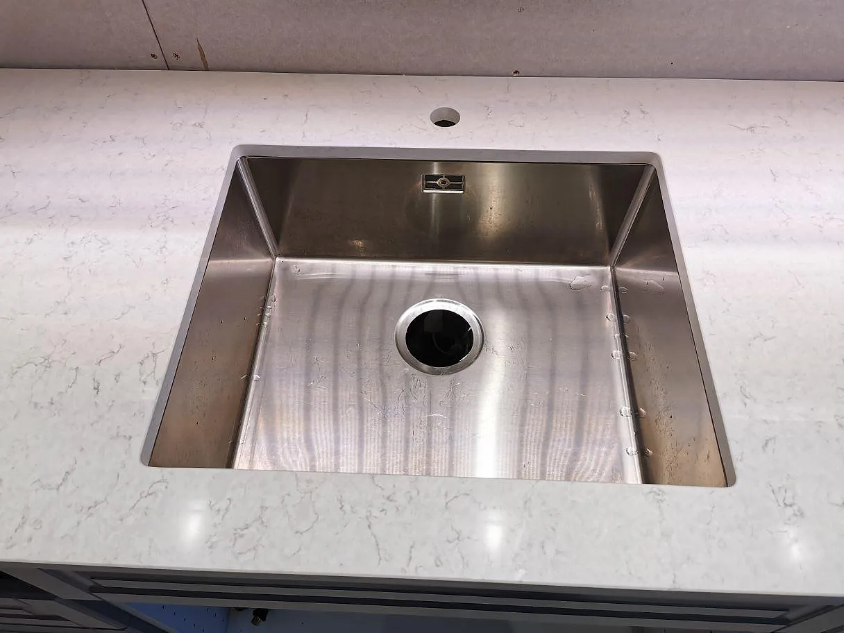 Underlimmad rostfri diskho infälld i polerad vit Silestone Snowy Ibiza köksbänkskiva i ett kök i Sjöbo.