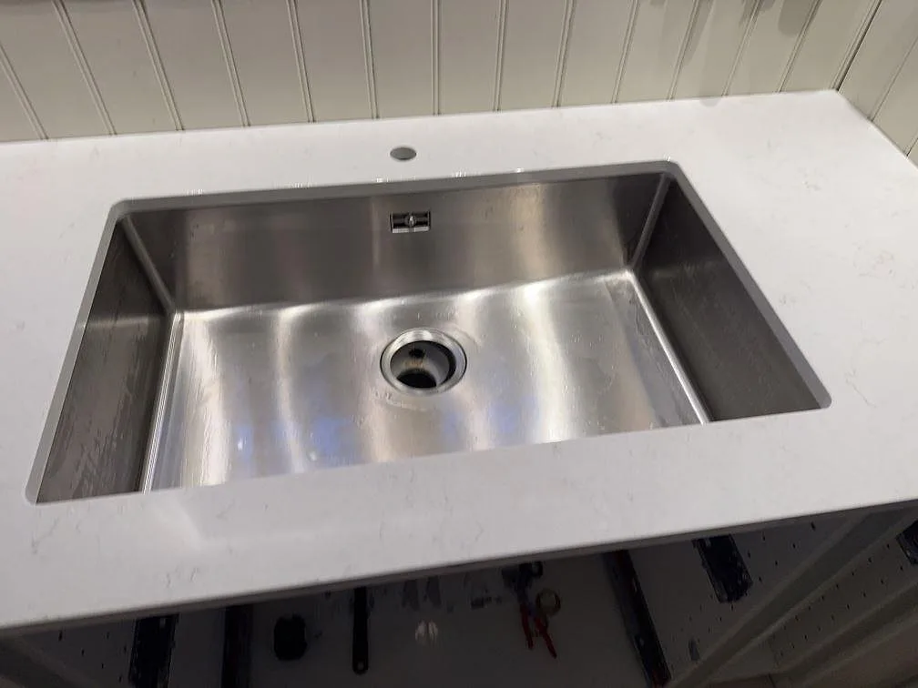 Närbild på rostfri diskho i polerad Silestone Snowy Ibiza kompositbänkskiva i Sjuntorp.