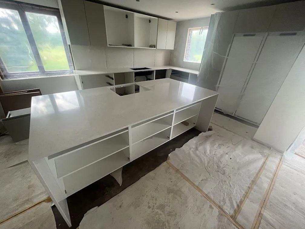 Stor köksö och köksbänkskivor i vit Silestone Snowy Ibiza, polerad kvartskomposit, i ett kök under montering i Skärblacka.