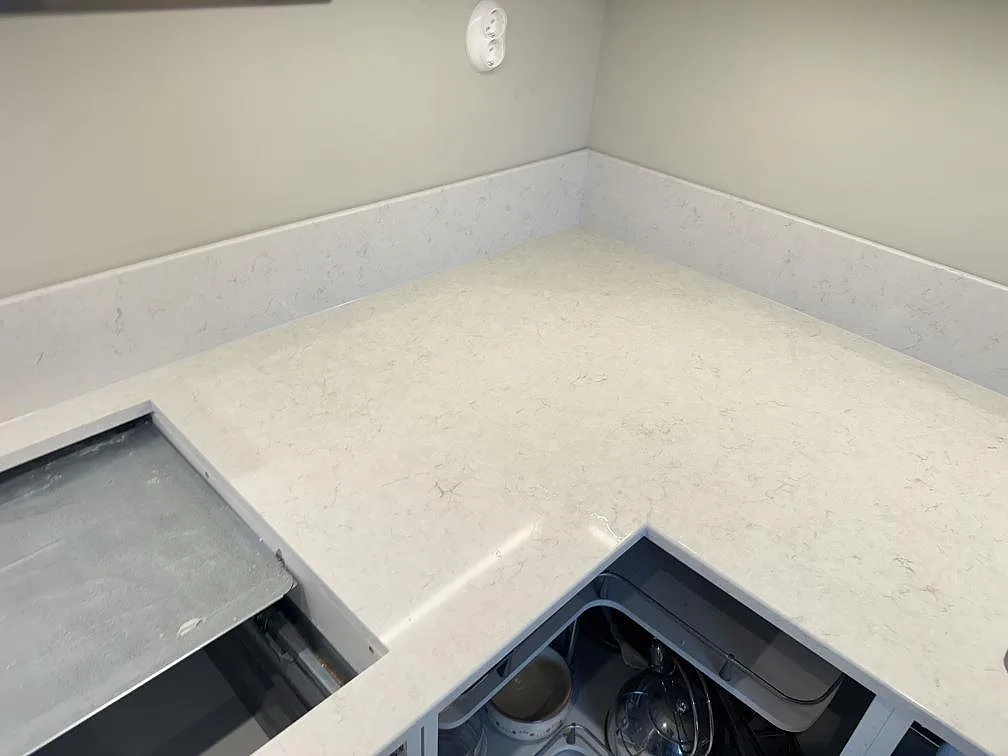 Vinkelbänk i vit Silestone Snowy Ibiza, polerad, i ett L-format hörnkök i Skanör, med urtag för häll och låg uppvikt stänkkant under montering.
