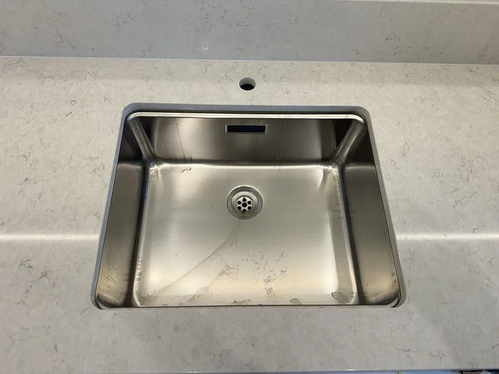Närbild ovanifrån på underlimmad rektangulär rostfri diskho i vit Silestone Snowy Ibiza, polerad, i ett kök i Skanör.