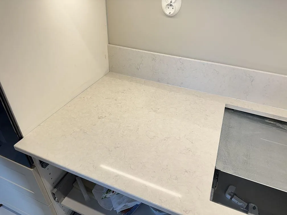 Köksbänkskiva i vit Silestone Snowy Ibiza, polerad, i hörnläge med urtag för infälld häll och låg stänkkant i ett kök i Skanör.