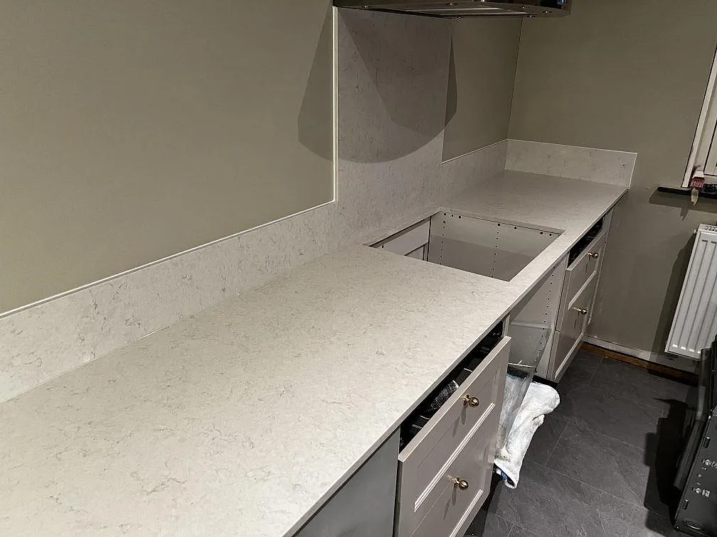 U-format kök i Skummeslövsstrand med polerad köksbänkskiva i Silestone Snowy Ibiza, låg stänkkant och grå/taupe köksinredning under montering.