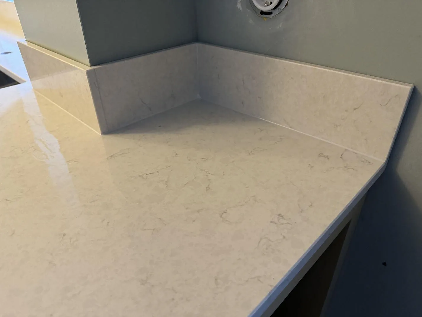 Närbild på polerad Silestone Snowy Ibiza med uppvikt stänkkant och ljus ådring vid köksvägg i Skurup.