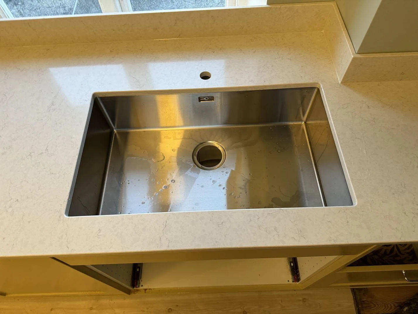 Närbild på underlimmad rostfri diskho i polerad Silestone Snowy Ibiza med blandarhål och stänkskydd i Skurup.