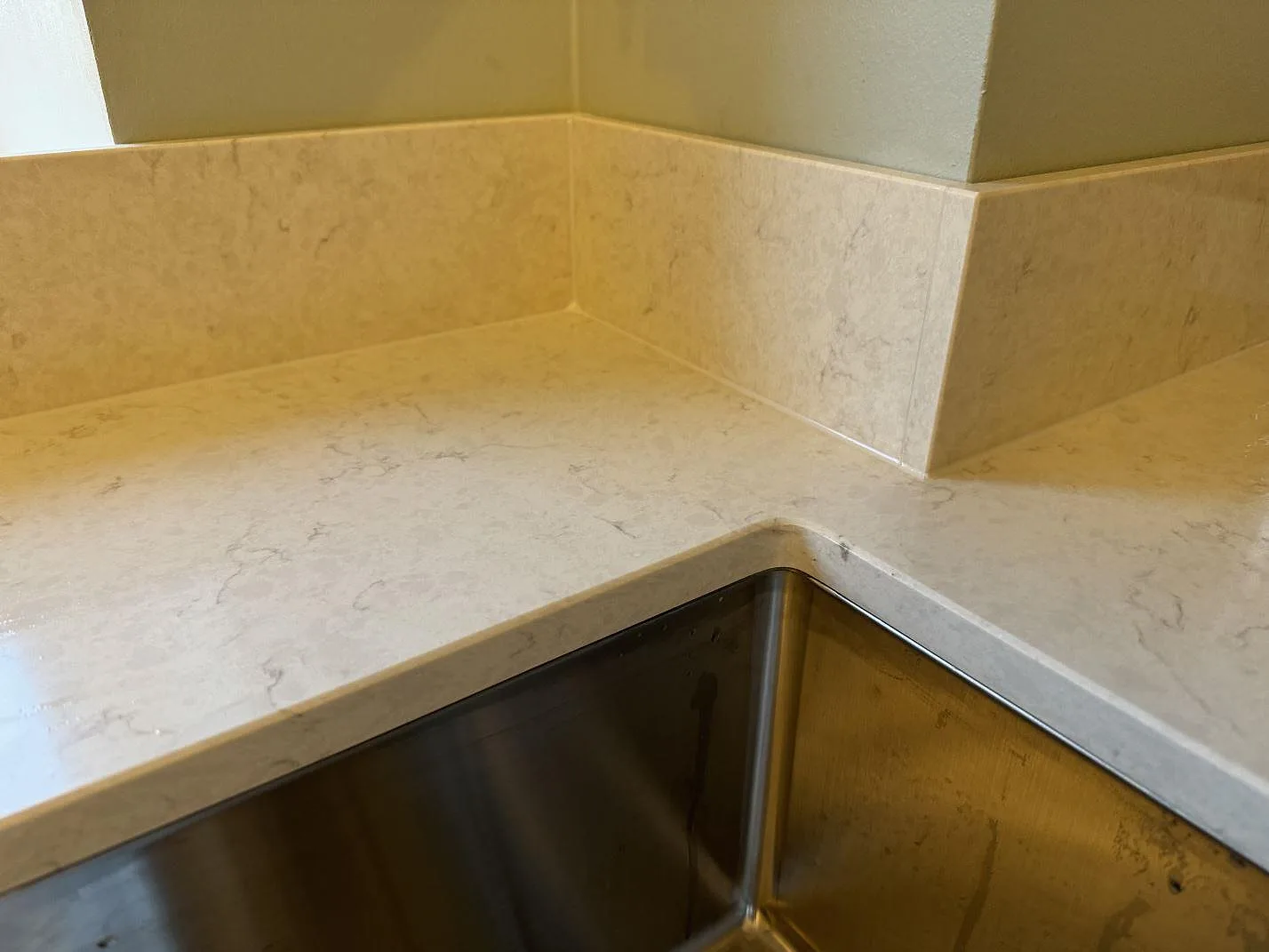 Detalj av rostfri underlimmad diskho, polerad Silestone Snowy Ibiza och 12 mm stänkskydd runt hörn i Skurup.