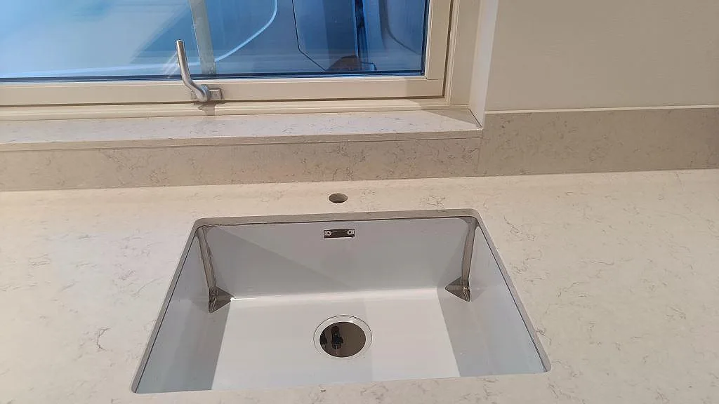 Rak detaljbild av underlimmad diskho i Silestone Snowy Ibiza med ljus ådring och polerad yta i Skurup.