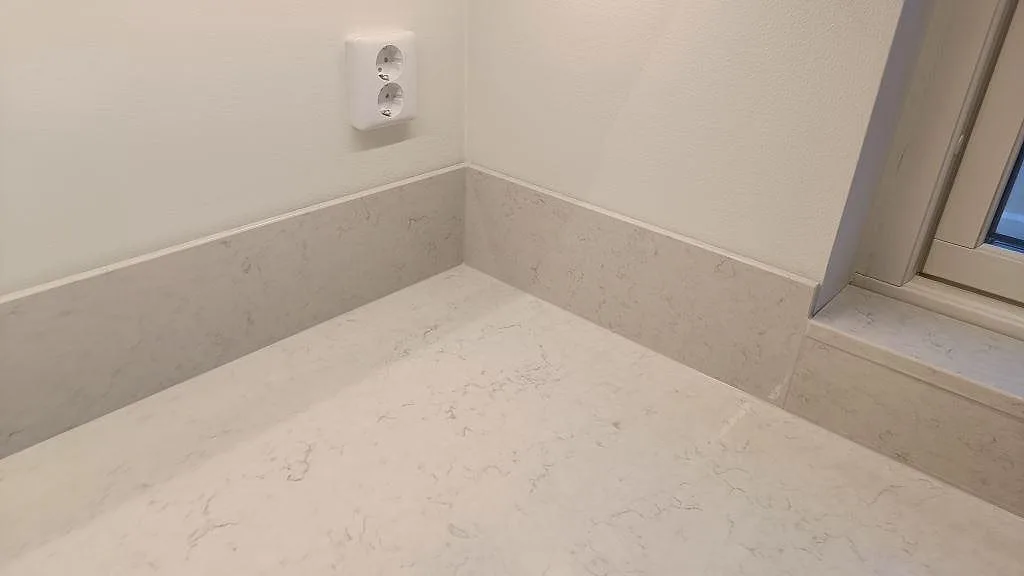 Hörn av bänkskiva och stänkskydd i polerad Silestone Snowy Ibiza vid fönster i Skurup.