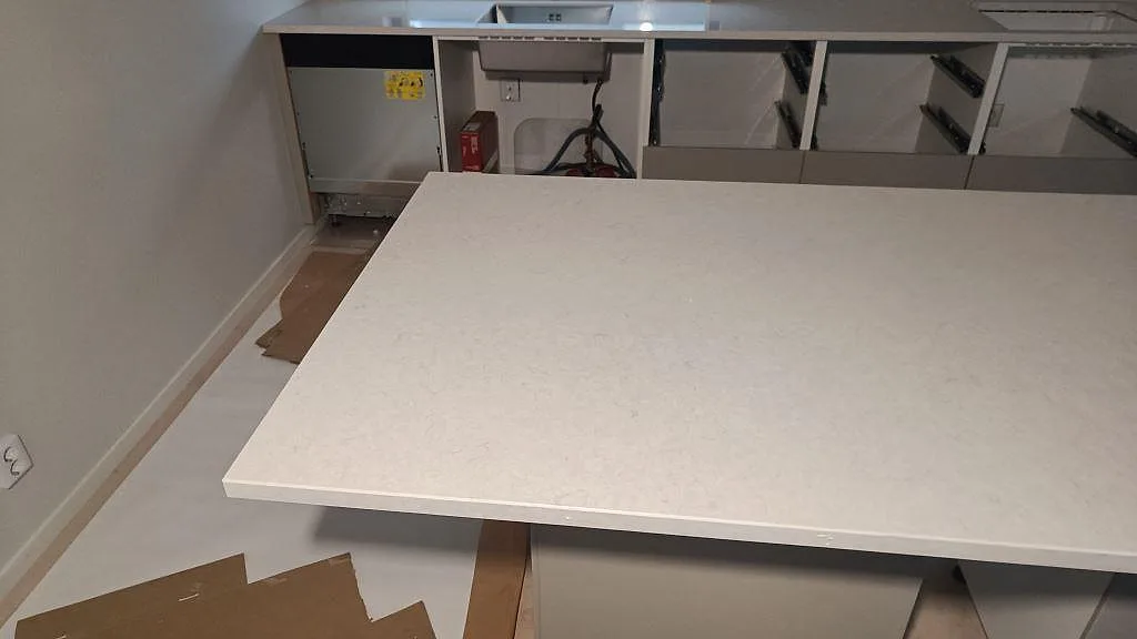 Närbild på polerad Silestone Snowy Ibiza över köksön med ljus kompositstruktur och bänkrad i bakgrunden i Skurup.