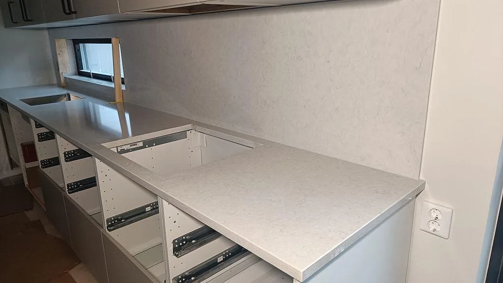 Bakre köksbänkskiva i polerad Silestone Snowy Ibiza med väggpanel och urtag i ett kök i Skurup.
